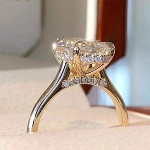 May include: A gold engagement ring with a large, oval-cut diamond as the centerpiece. The diamond is surrounded by a halo of smaller stones, and the band features additional accent stones. The ring is set in a gold band.