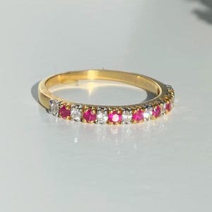 May include: A gold band ring with a row of alternating ruby and diamond stones.