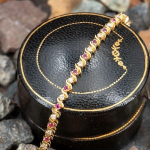 Puede incluir: Un brazalete de oro con un delicado diseño trenzado engastado con piedras redondas de rubí y diamantes alternas.