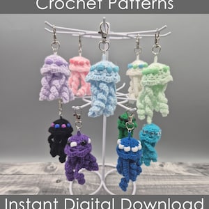 May include: A display of handmade crochet jellyfish keychains in various colors, including purple, pink, blue, green, and white. The keychains are suspended from a white metal stand. The text "Crochet Patterns" and "Instant Digital Download" are displayed.