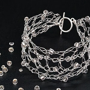 May include: A silver bracelet with a toggle clasp and clear glass beads woven into the chain.