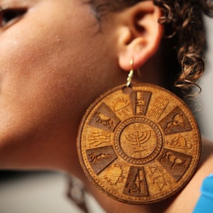 May include: Large wooden earrings with a circular design featuring a menorah and other symbols. The earrings are brown and have a natural wood finish.