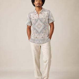 May include: A short-sleeved shirt with a split neckline featuring a detailed blue, brown, and white paisley-inspired pattern, paired with straight-leg beige trousers and light-colored shoes. The shirt has a straight hem and a relaxed fit.