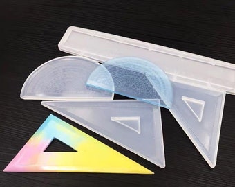 May include: A set of four clear plastic protractors and rulers, including a long ruler, two protractors, and a triangle ruler. The protractors have degree markings and the triangle ruler has a 45-degree angle and a 90-degree angle.