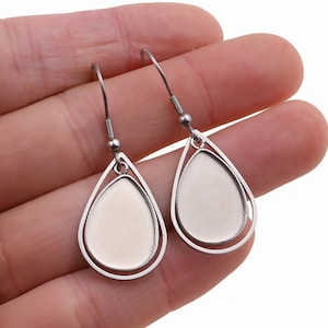 May include: A pair of silver teardrop-shaped earrings with a smooth, round, blank center for adding a custom design. The earrings have a simple, elegant design.