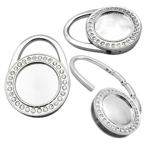 Könnte beinhalten: Ein silberfarbener Haken aus Metall mit einem runden, mit klaren Kristallen besetzten Design. Der Haken ist faltbar und kann zum Aufhängen von Gegenständen verwendet werden.