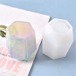 May include: Two hexagonal silicone molds for resin casting. One mold is filled with a rainbow iridescent resin, the other is empty.