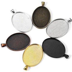 May include: Five oval-shaped metal pendant trays with different finishes: silver, gold, black, copper, and antique bronze. Each tray has a textured surface and a loop at the top for hanging.