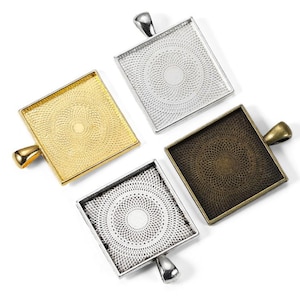 Könnte beinhalten: Vier quadratische Anhänger-Tabletts in Gold, Silber, Bronze und Gunmetal. Jedes Tablett hat ein dekoratives, kreisförmiges Filigranmuster in der Mitte und eine kleine Schlaufe zum Anbringen einer Kette oder eines Bügels. Die Tabletts werden auf weißem Hintergrund angezeigt.