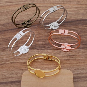 Puede incluir: Cuatro pulseras de metal con un espacio redondo abierto para un camafeo u otro adorno. Las pulseras son de plata, oro, oro rosa y latón antiguo.