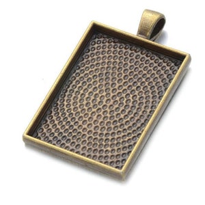 May include: A bronze-colored metal pendant tray with a textured surface. The tray is rectangular and has a loop at the top for hanging.