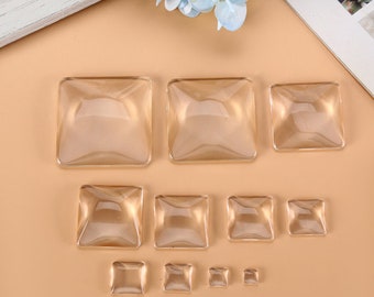 Pode incluir: Conjunto de cabochões quadrados de vidro transparente de vários tamanhos. Os cabochões são todos planos de um lado e têm uma parte superior abobadada.