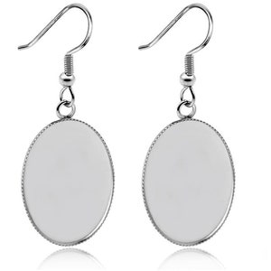 Könnte beinhalten: Ein Paar silberne ovale Ohrringe mit einer glatten, weißen Oberfläche. Die Ohrringe haben ein schlichtes, elegantes Design und sind perfekt für den Alltag.