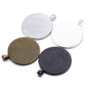 Op de afbeelding: Vier ronde metalen hangerbases in zilver, brons en zwart. Elke basis heeft een getextureerd oppervlak en een lus aan de bovenkant om een ​​ketting of koord aan te bevestigen.