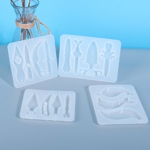 Könnte beinhalten: Vier weiße Silikonformen zum Herstellen von Kunsthandwerk aus Harz. Jede Form zeigt verschiedene Formen von Messern und Dolchen.