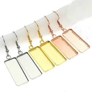 May include: Four pairs of silver, gold, and rose gold earrings with rectangular glass or resin inserts. The earrings are dangle style with a hook closure.