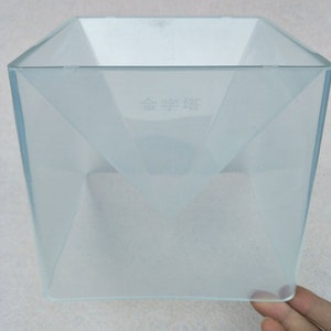 May include: A clear plastic square-shaped container with a funnel-shaped opening at the top. The container has the text "金字塔" printed on the side.