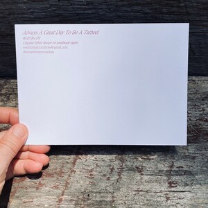 May include: A white card with the text "Always A Great Day To Be A Tarheel" in maroon. Additional text includes "#GDTBATH", and contact information for sweettomatocreations. The card is held against a weathered wooden surface.