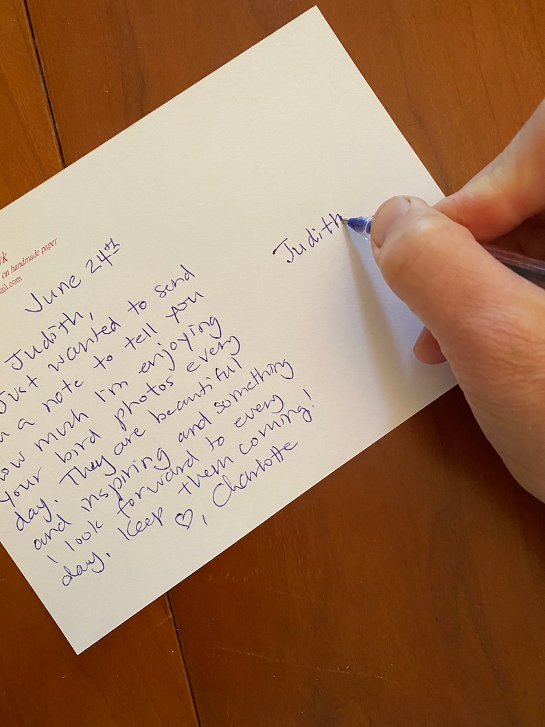 May include: A handwritten note on white paper with blue ink. The text includes the name "Judith" and a message about enjoying bird photos. The date "June 24th" is also visible. The note is being written with a blue pen.