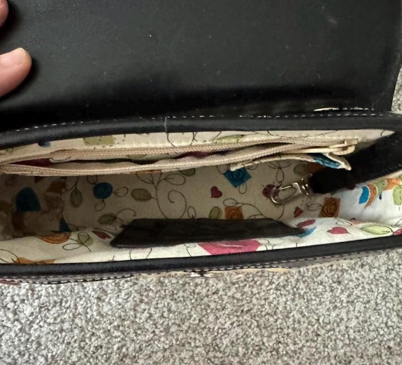 May include: Open black leather handbag with a patterned interior. The interior fabric features colorful floral and geometric designs. The bag has multiple compartments and a silver-colored clasp.