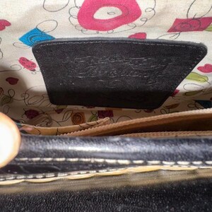 May include: Black leather handbag with a patterned interior. The interior features a floral design with pink, blue, and green accents. A black leather tag is visible inside the bag.