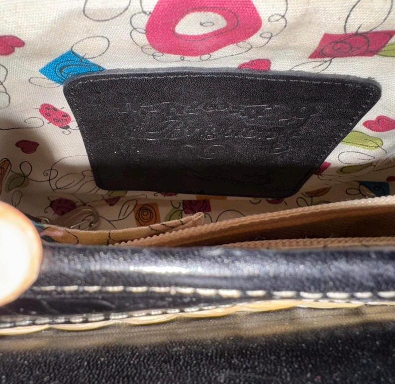 May include: Black leather handbag with a patterned interior. The interior features a floral design with pink, blue, and green accents. A black leather tag is visible inside the bag.