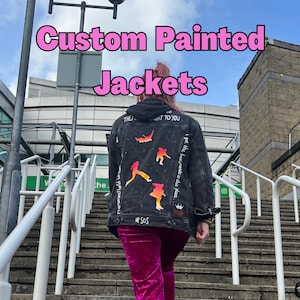 May include: A black denim jacket with custom hand-painted designs. The jacket features a colourful illustration of figures and the text "THEY", "NT TO YOU", "I got the boorgronds in this place", and "SOS".