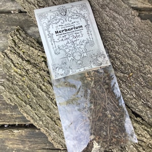 May include: A clear plastic bag filled with dried herbs labeled "Herbarium Dried Herbs and Flowers Saint John's Wort" on a white label with a decorative border.