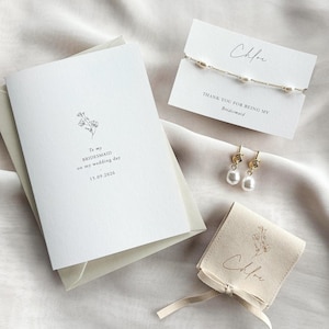 May include: A selection of wedding accessories, including a card with the text "To my BRIDESMAID on my wedding day 15.09.2026", a bracelet, earrings, and a small pouch. The bracelet and earrings feature pearls. The pouch and card are labeled "Chloe".