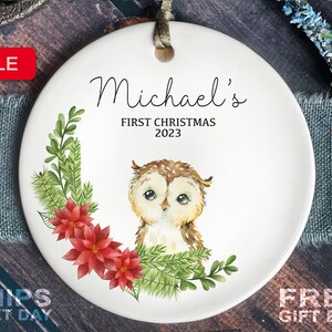 May include: White ceramic Christmas ornament with a watercolor illustration of an owl, a red poinsettia, and green pine branches. The ornament is personalized with the text "Michael's First Christmas 2023".