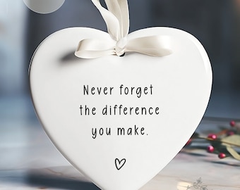 May include: White ceramic heart ornament with a white satin ribbon. The ornament has the text "Never forget the difference you make." and a small heart symbol.