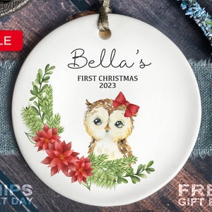 May include: White ceramic Christmas ornament with a watercolor illustration of an owl wearing a red bow. The ornament has the text "Bella's First Christmas 2023" on it.