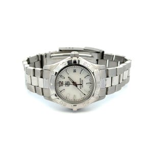 Könnte beinhalten: Eine silberfarbene TAG Heuer Aquaracer Uhr mit weißem Zifferblatt. Die Uhr verfügt über ein Edelstahlarmband und eine Datumsanzeige auf 3 Uhr. Wasserdicht bis 300 Meter.