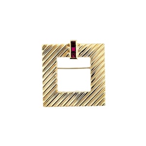 Può includere: Un pendente quadrato color oro con un motivo a righe diagonali strutturate. Il pendente ha un'apertura rettangolare al centro e una piccola gemma rossa rettangolare nella parte superiore. Il gioiello è posto su uno sfondo bianco.