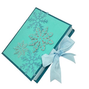 Op de afbeelding: Een tealblauwe cadeaudoos met een lichtblauw lint. De doos is versierd met zilveren glitter sneeuwvlokken.