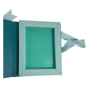 Op de afbeelding: Een lichtblauwe cadeaudoos met een lichtblauw lint. De doos is open en de binnenkant is bekleed met lichtgroen papier.