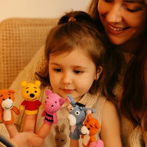 May include: A child and an adult are looking at a book while the child wears a set of colorful finger puppets. The puppets include a yellow bear, a pink pig, a blue donkey, an orange tiger, and a brown rabbit. The puppets are made of yarn.