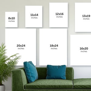 May include: A white wall with nine different sized white frames, each with black text indicating the size of the frame in inches. The frames are arranged in a grid pattern. The frames are hanging on a white wall. There is a green couch in the foreground with two blue throw pillows.