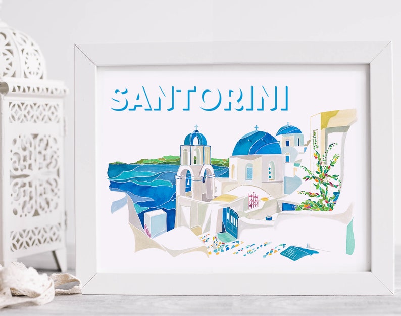 K&ouml;nnte beinhalten: Ein wei&szlig;er gerahmter Druck mit dem Wort "SANTORINI" in blauen Buchstaben. Der Druck zeigt eine Aquarellillustration eines wei&szlig;en Geb&auml;udes mit blauen Kuppeln und einem blauen Meer im Hintergrund.