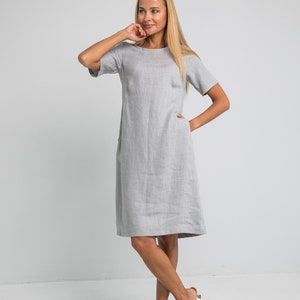 May include: A gray linen dress with short sleeves and pockets. The dress is knee-length and has a relaxed fit.