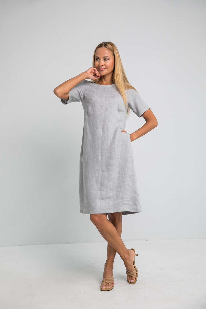 May include: A gray linen dress with short sleeves and pockets. The dress is knee-length and has a relaxed fit.