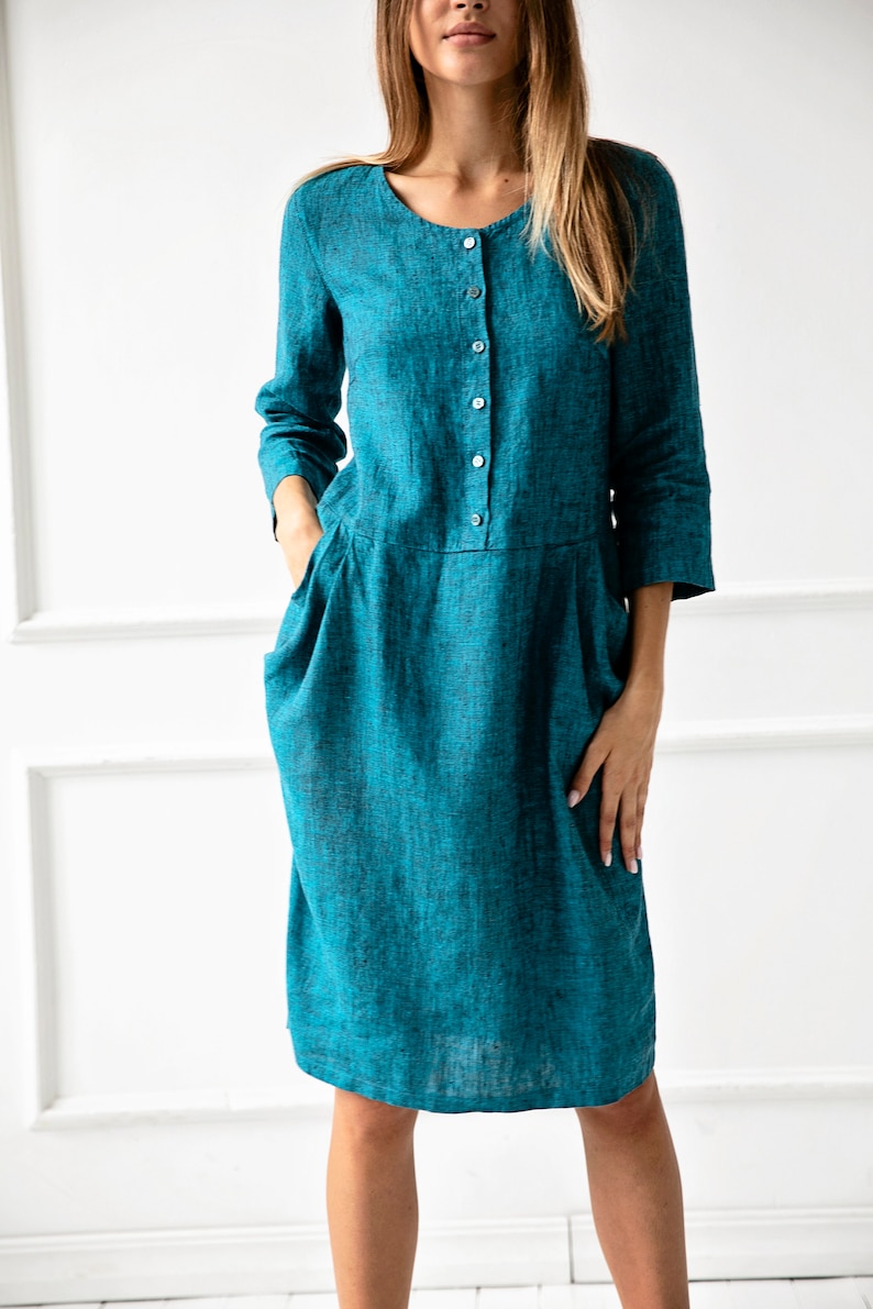 May include: A teal linen dress with a button-up front and pockets. The dress has a relaxed fit and a midi length.