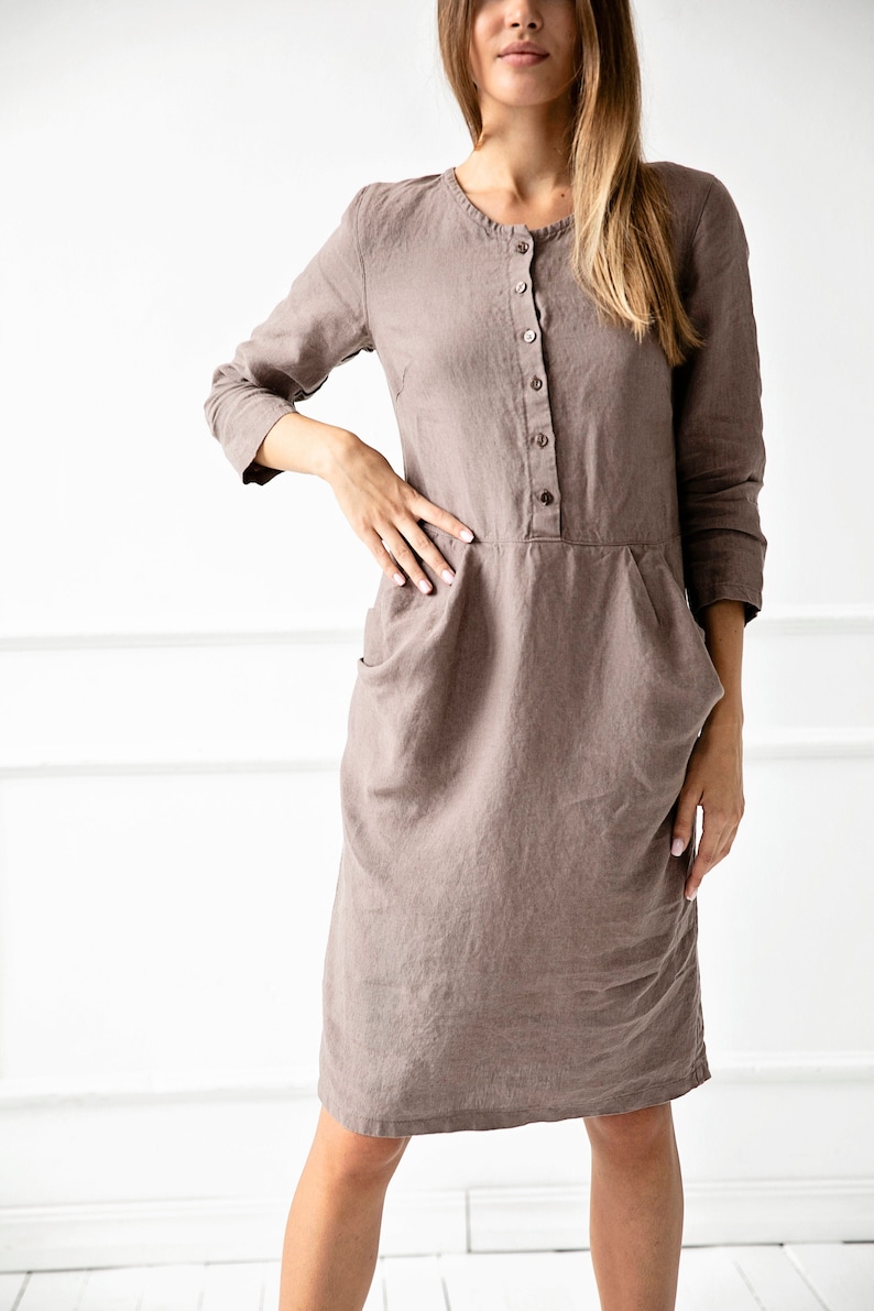 May include: A brown linen dress with a button-up front and pockets. The dress has a relaxed fit and is knee-length.