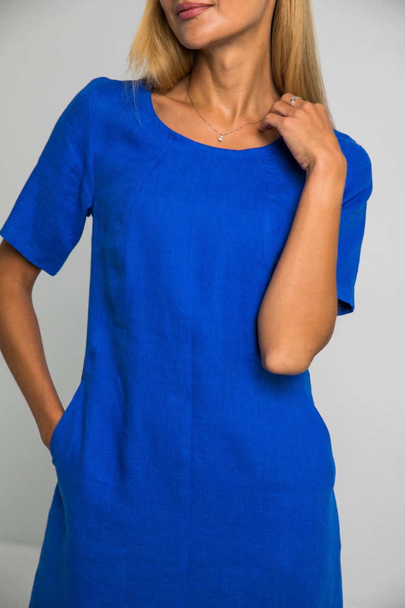 May include: A royal blue linen dress with short sleeves and a scoop neck. The dress has two pockets on the front.
