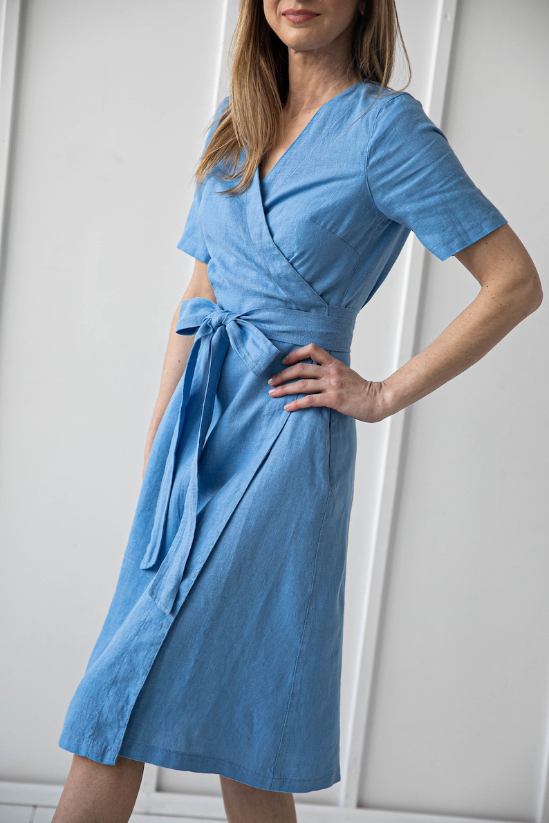 May include: A light blue linen wrap dress with short sleeves and a tie belt.
