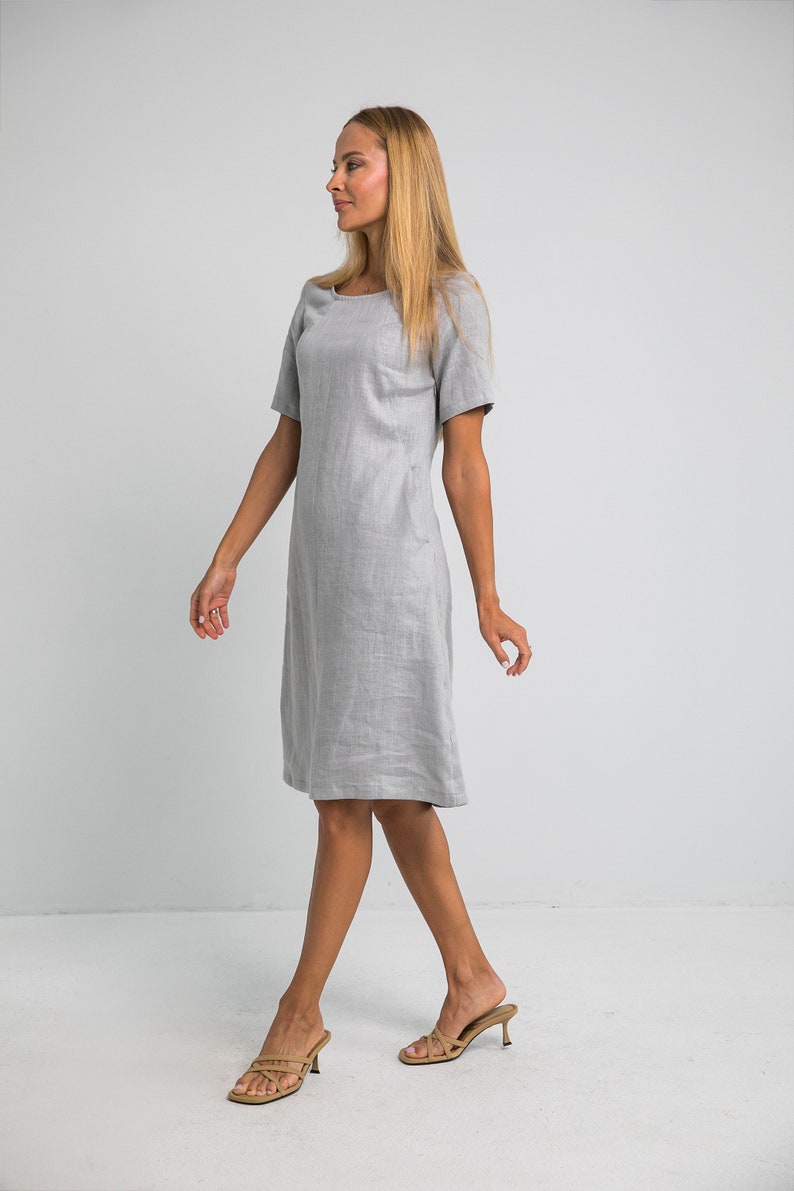 May include: A gray linen dress with short sleeves and a scoop neck. The dress is knee-length and has a relaxed fit.