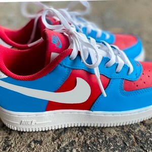 May include: Blue and red low-top sneakers with a white swoosh logo and white laces. The shoes have a white sole and the word "NIKE" is printed on the side.