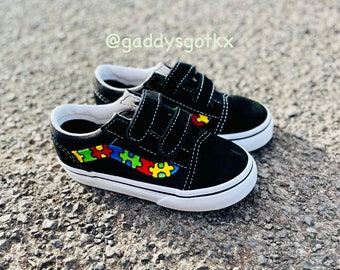 May include: Black canvas shoes with velcro closures and a colorful puzzle piece design on the side. The shoes are on a gray gravel surface. @gaddysgotkx