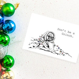 May include: A black and white illustration of a dog wrapped in Christmas lights with the text "Don't be a Grinch."