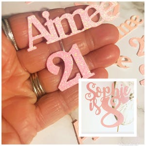 Może przedstawiać: Różowe błyszczące ozdoby na tort z imionami "Aimee" i "Sophie" oraz liczbami "21" i "8".